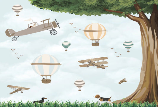 Papel tapiz infantil con globos aerostáticos, avionetas vintage, perritos en el pasto y un gran árbol.